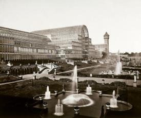 Photographie en noir et blanc d'une architecture en verre et fer, jardins avec des jets d'eau